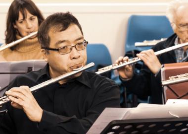 people arranged in seated rows playing the flute together in a community hall