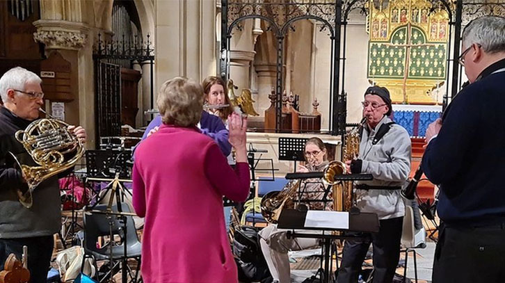 members of the orchestra standing, playing their instruments inside a church